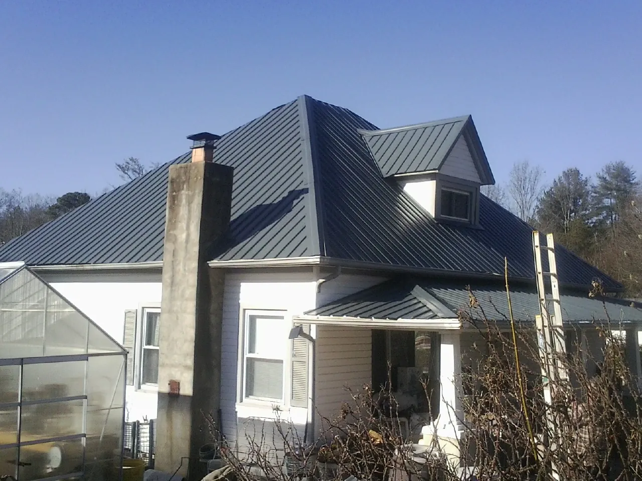Dark blue standing seam metal roof on a white farmhouse with dormer — Slate & Tile Roof Repair by Roofing Brothers in Bainbridge