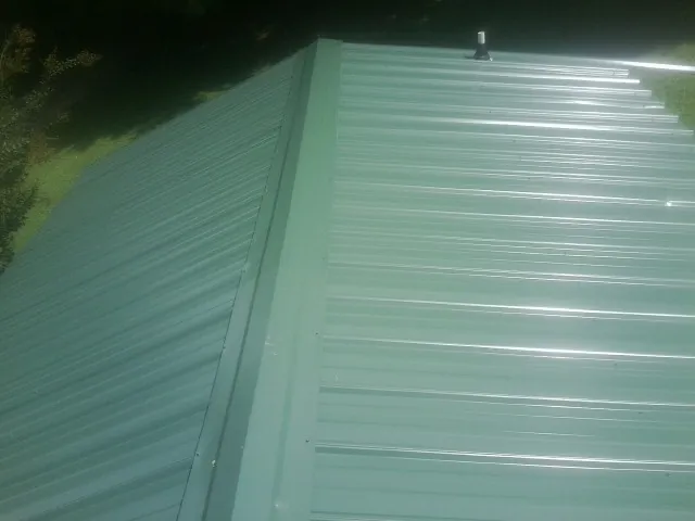 New green metal panels meeting at the ridge of a roof — Flat Roof Repair work by our crew in Bainbridge